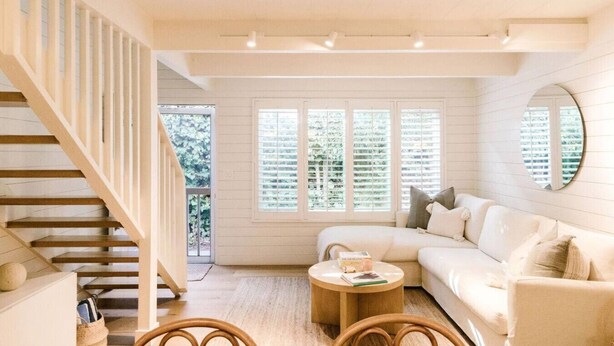 A spacious living room with a white sofa, a round coffee table, and a wooden staircase. - Darling Carpinteria Beach Getaway (Carpinteria)