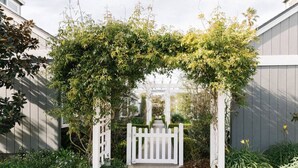 A white wooden archway with climbing plants, leading to a gated entrance. - Darling Carpinteria Beach Getaway (Carpinteria)