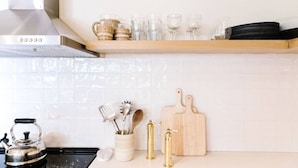 A kitchen with a stainless steel range hood, a wooden shelf with glassware, a kettle, a spice rack, and a cutting board. - Darling Carpinteria Beach Getaway (Carpinteria)