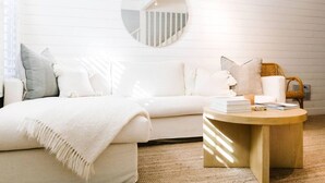 A modern, minimalist bedroom with a white sofa, a round mirror, and a wooden coffee table. - Darling Carpinteria Beach Getaway (Carpinteria)