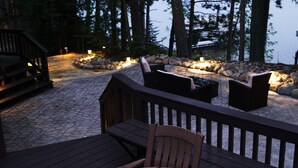 Une terrasse avec des sièges extérieurs et un chemin de pierre menant à un espace aménagé autour d’un foyer, le tout entouré de rochers.