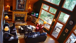 Un salon chaleureux avec une cheminée, des sièges confortables et de grandes fenêtres donnant sur l’extérieur.
