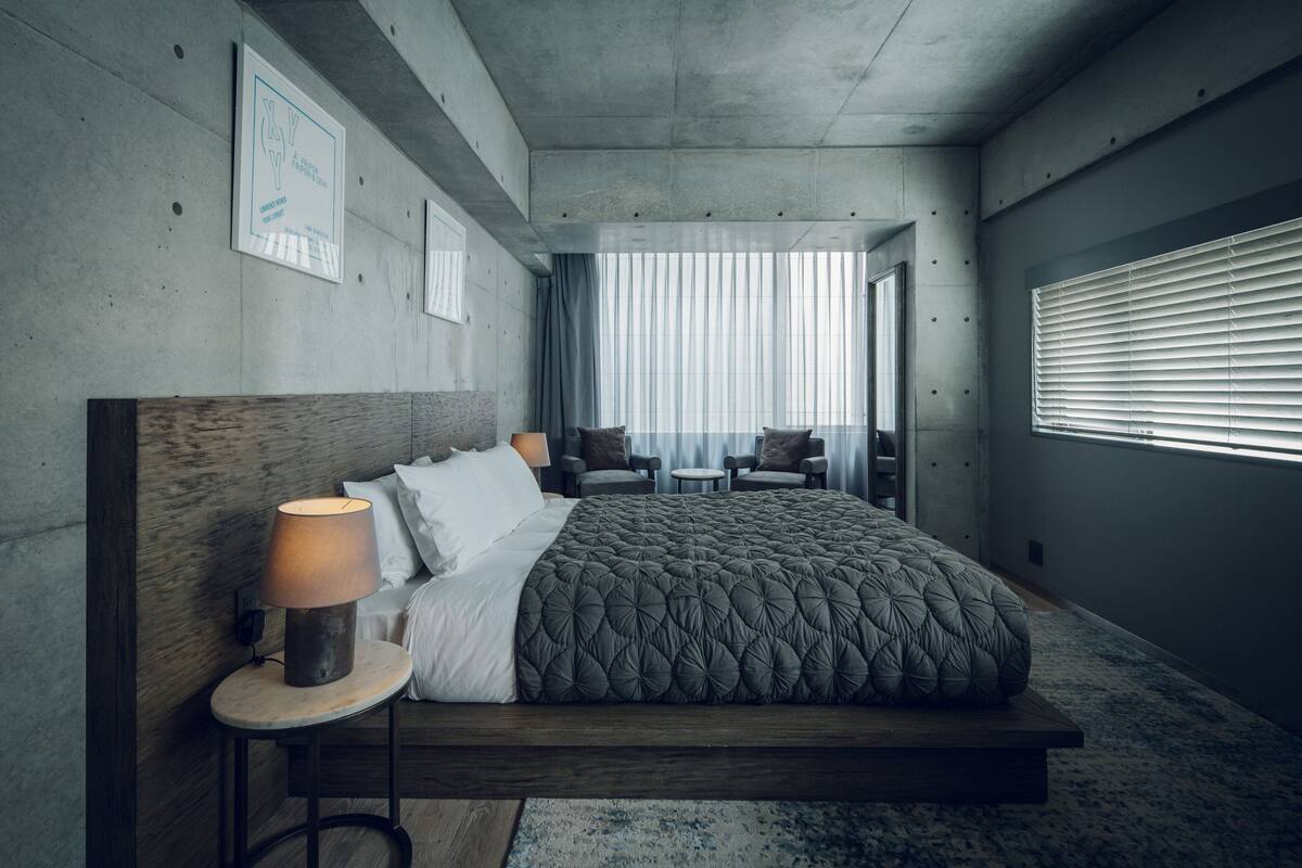 A modern hotel room with a large bed, a bedside table with a lamp, a small round table, and a chair.