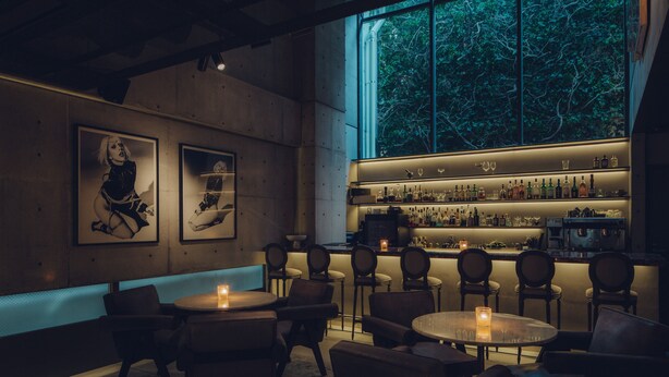 A dimly lit bar area with multiple seating options, a bar counter with various bottles, and framed artwork on the walls. - Node Hotel (Kyoto)