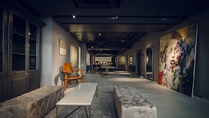 A spacious hallway with a long table, two cushioned seating areas, and a large abstract painting on the right wall. - Node Hotel (Kyoto)