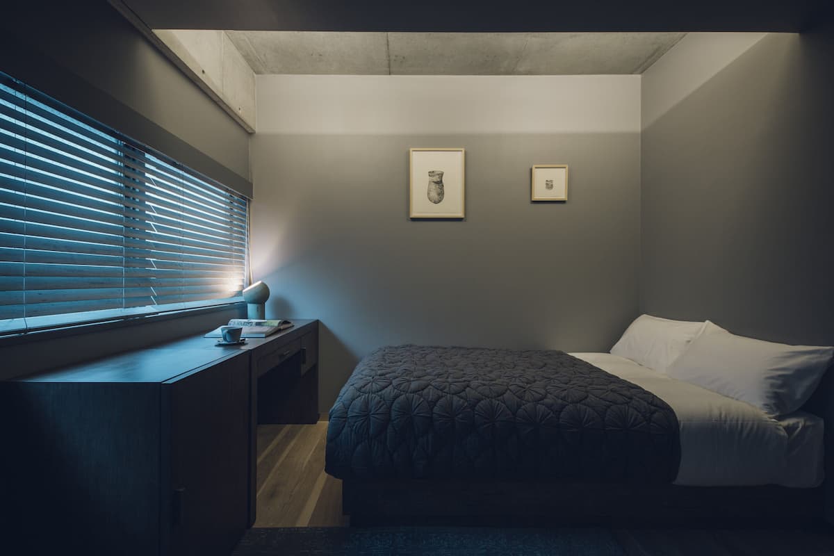 A bedroom with a bed, a desk, and two framed pictures on the wall.