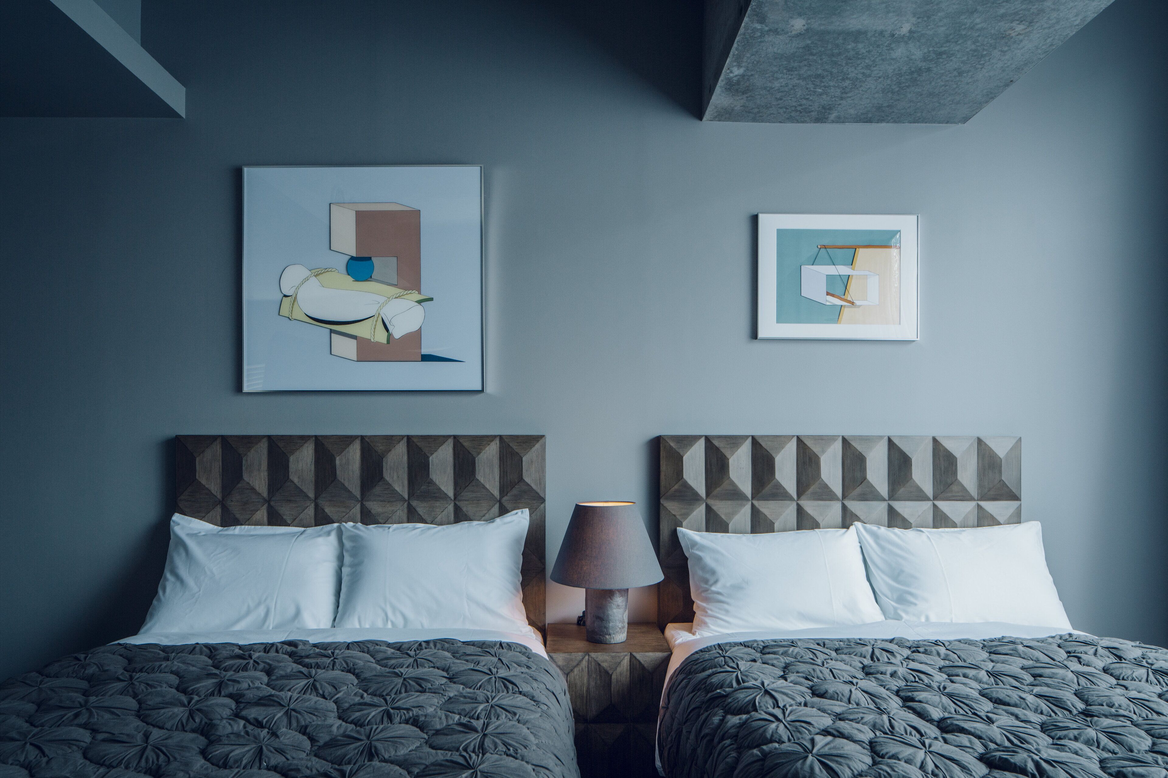 A double bed with a geometric-patterned headboard, a bedside lamp, and two framed artworks on the wall.
