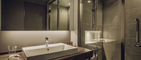 A modern bathroom with a large mirror, a sink, and a glass-enclosed shower.