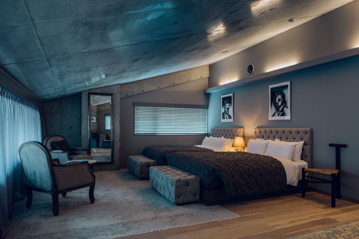 A bedroom with a large bed, a chair, a bench, and a mirror.