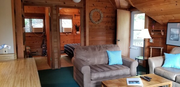 A cozy cabin interior with a wooden interior, a sofa, a coffee table, and a door leading to a balcony.
