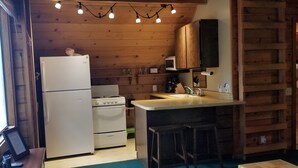 A compact kitchen with wooden walls, a white refrigerator, a stove, and a small bar area.
