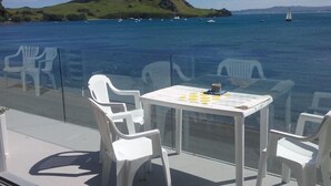Ein Tisch mit Stühlen, die auf eine malerische Meereslandschaft ausgerichtet sind, ein Schachbrett auf dem Tisch und ein Glasgeländer.