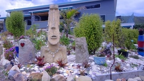 Ein modernes Haus mit Garten, das eine Steinskulptur, Kübelpflanzen und verschiedene Steine zeigt.