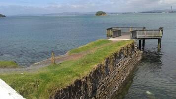 Una propiedad frente al agua con un área verde, un muro de contención de piedra y un muelle de madera que se adentra en el agua.