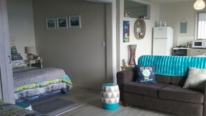 Ein kompakter Wohnbereich mit Bett, Sofa, kleinem Tisch und Küchenzeile.