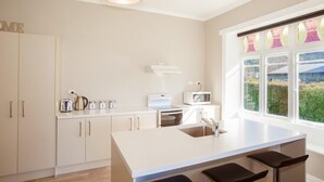 A modern kitchen with white cabinetry, a central island with seating, a microwave, a kettle, and a toaster. - Lake Villa 3 Bedroom in Kingston (Kingston)