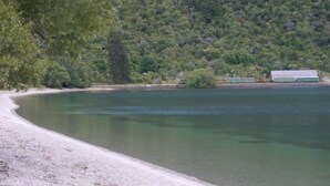 A serene lakeside scene with a sandy beach and a backdrop of dense green forest. - Lake Villa 3 Bedroom in Kingston (Kingston)