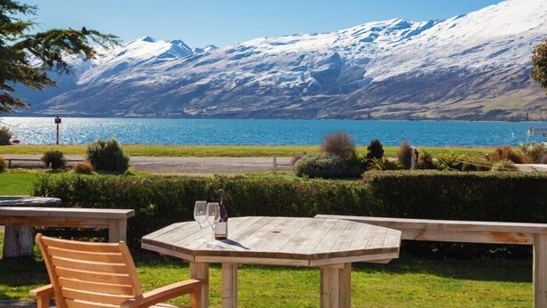 A wooden table with two chairs and a bottle of wine, overlooking a lake with a snow-capped mountain in the background. - Lake Villa 3 Bedroom in Kingston (Kingston)