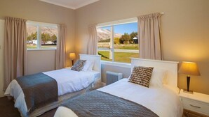 A hotel room with two beds, beige curtains, a view of a mountain and a building, and a window with a view of a field. - Lake Villa 3 Bedroom in Kingston (Kingston)