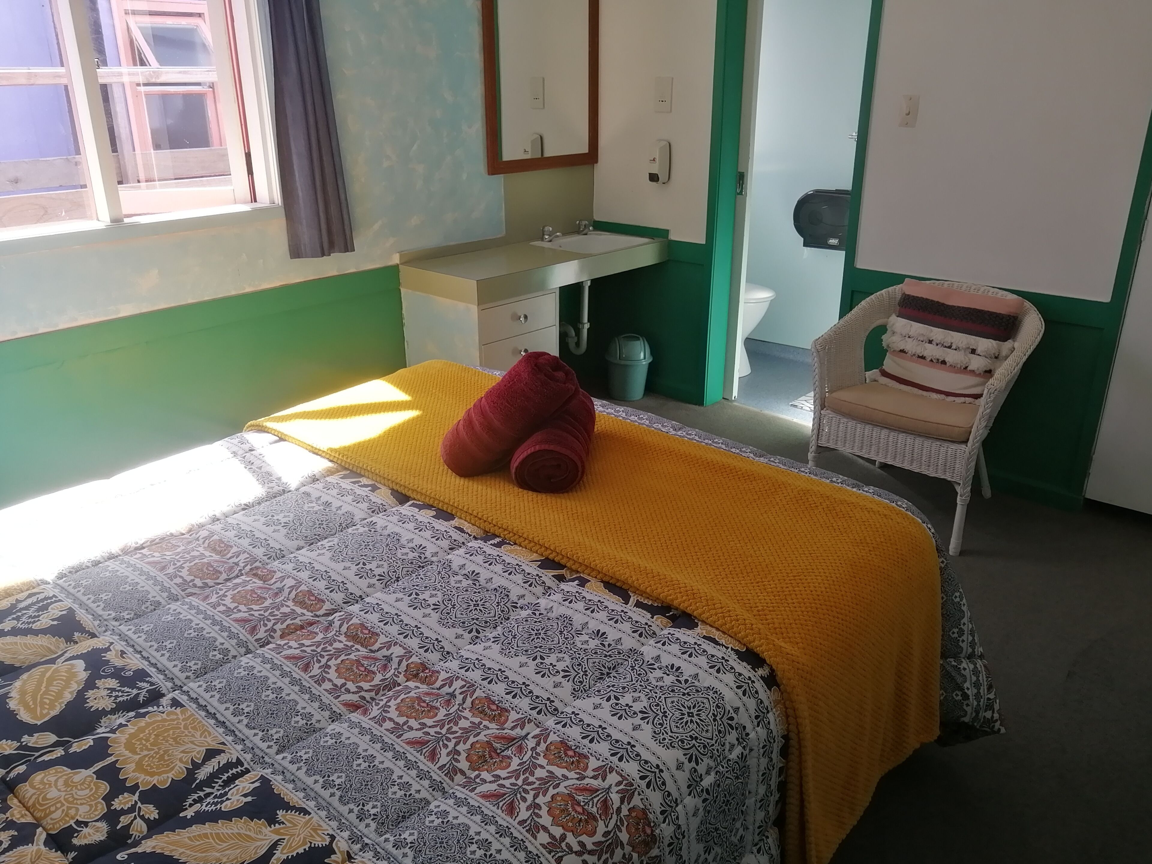 Um quarto com uma cama, uma cadeira, uma escrivaninha e uma janela.