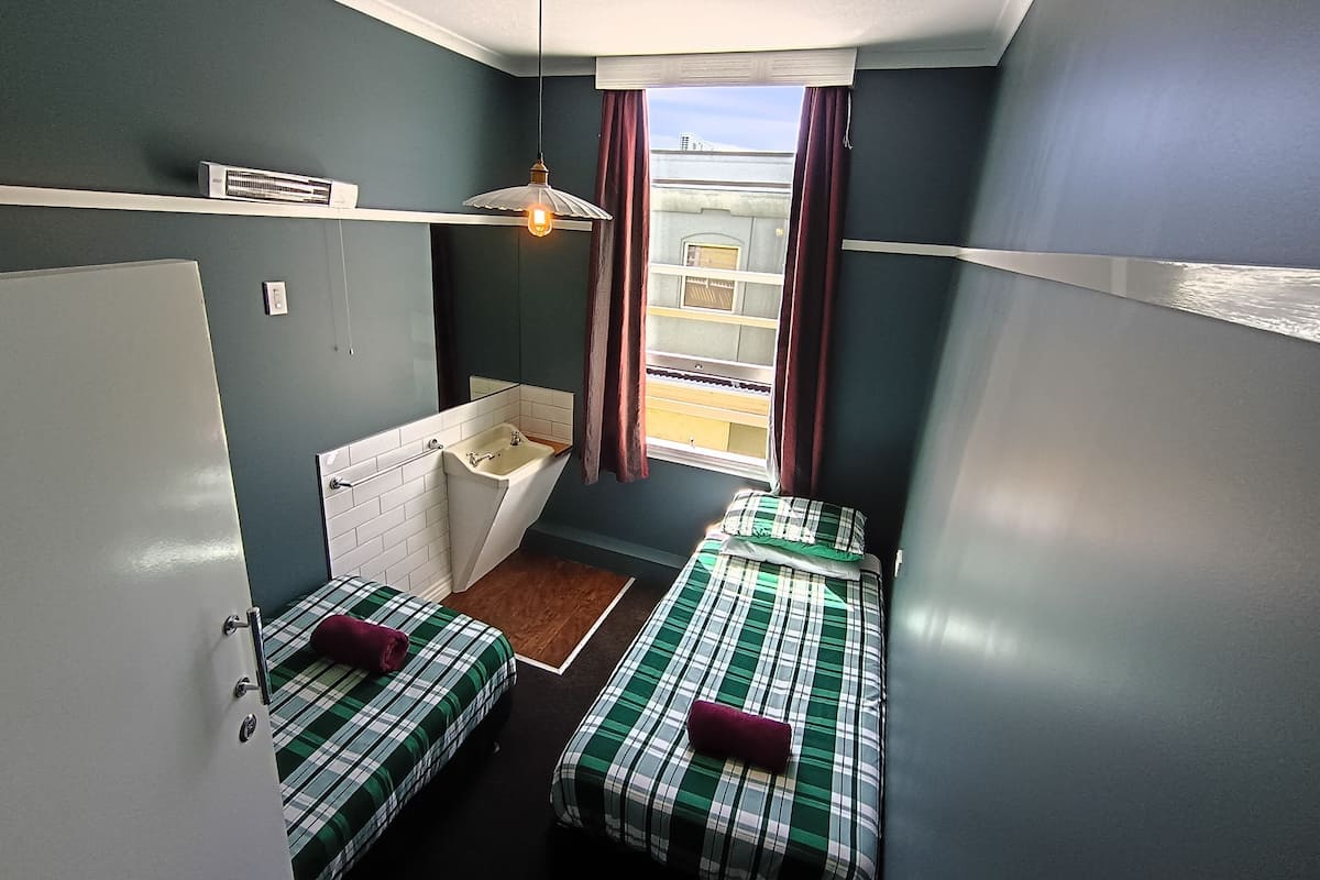 A small room with two beds, a window, a sink, and a ceiling fan.