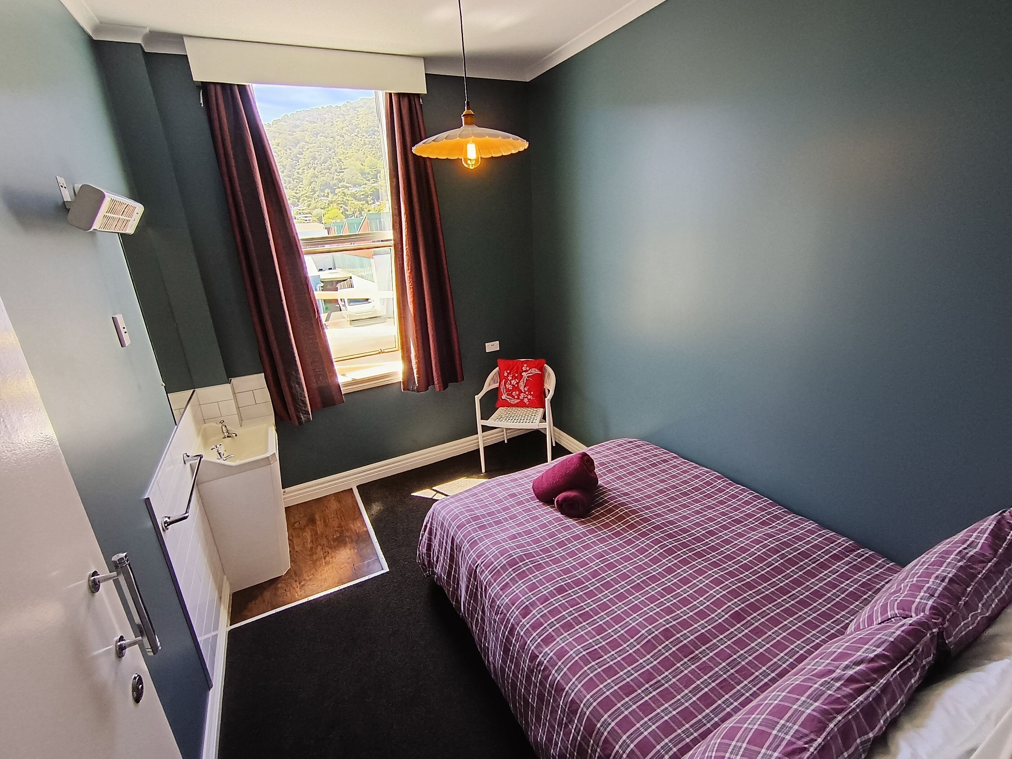 A bedroom with a bed, a window, a chair, and a sink.