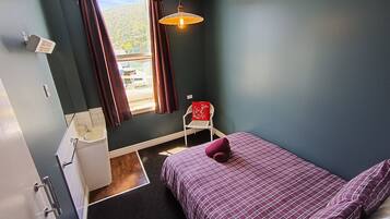 A bedroom with a bed, a window, a chair, and a sink.
