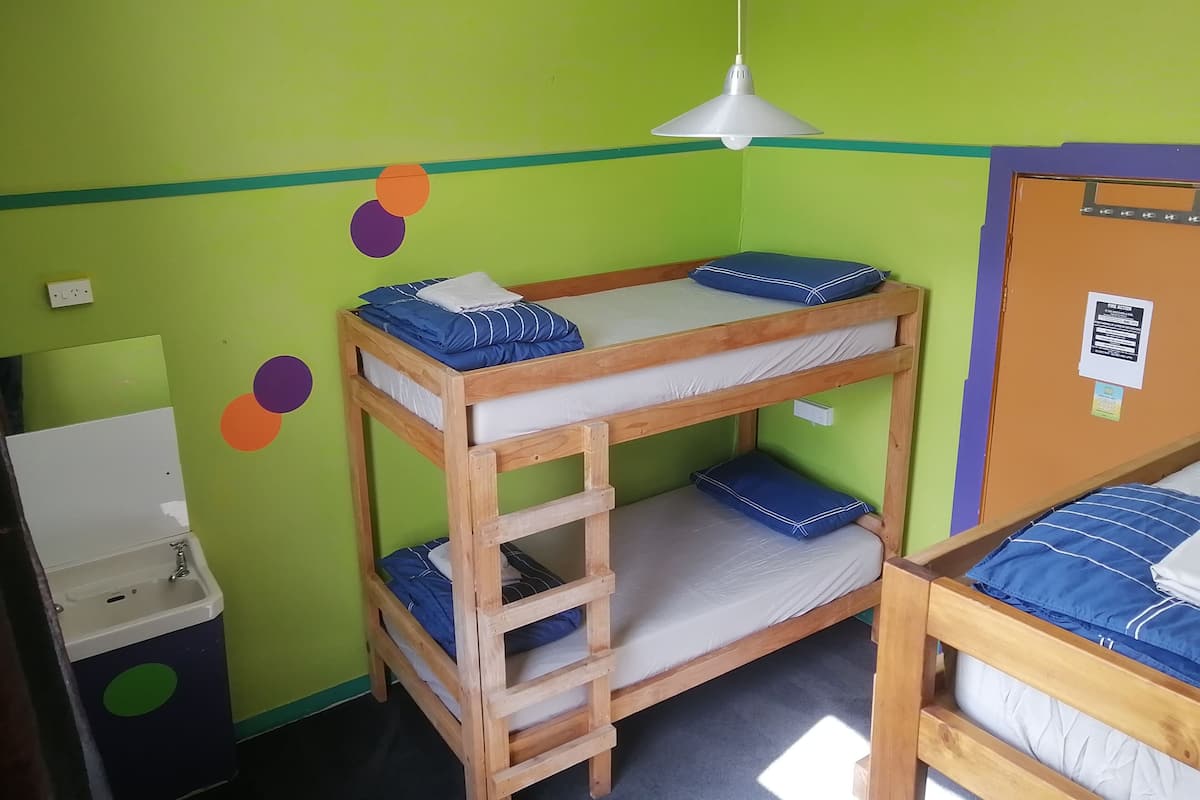 A bunk bed room with a wooden ladder, a white pendant light, and a small sink.