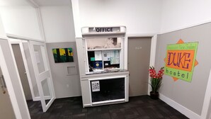 Un área de oficina con un mostrador de recepción, un panel informativo con un mapa y un cartel de Duke Hostel en Greyhound, Nueva Zelanda.