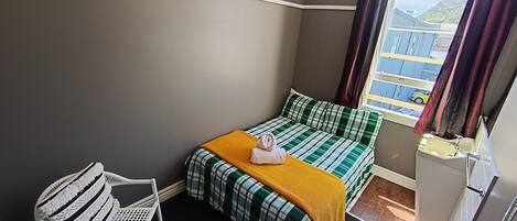Un dormitorio con una cama, una silla, un ventanal con cortinas y una lámpara colgante.