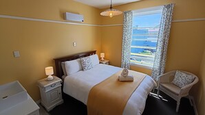Habitación de hotel con cama, lámparas de noche, ventana con vistas, una silla y una mesita.