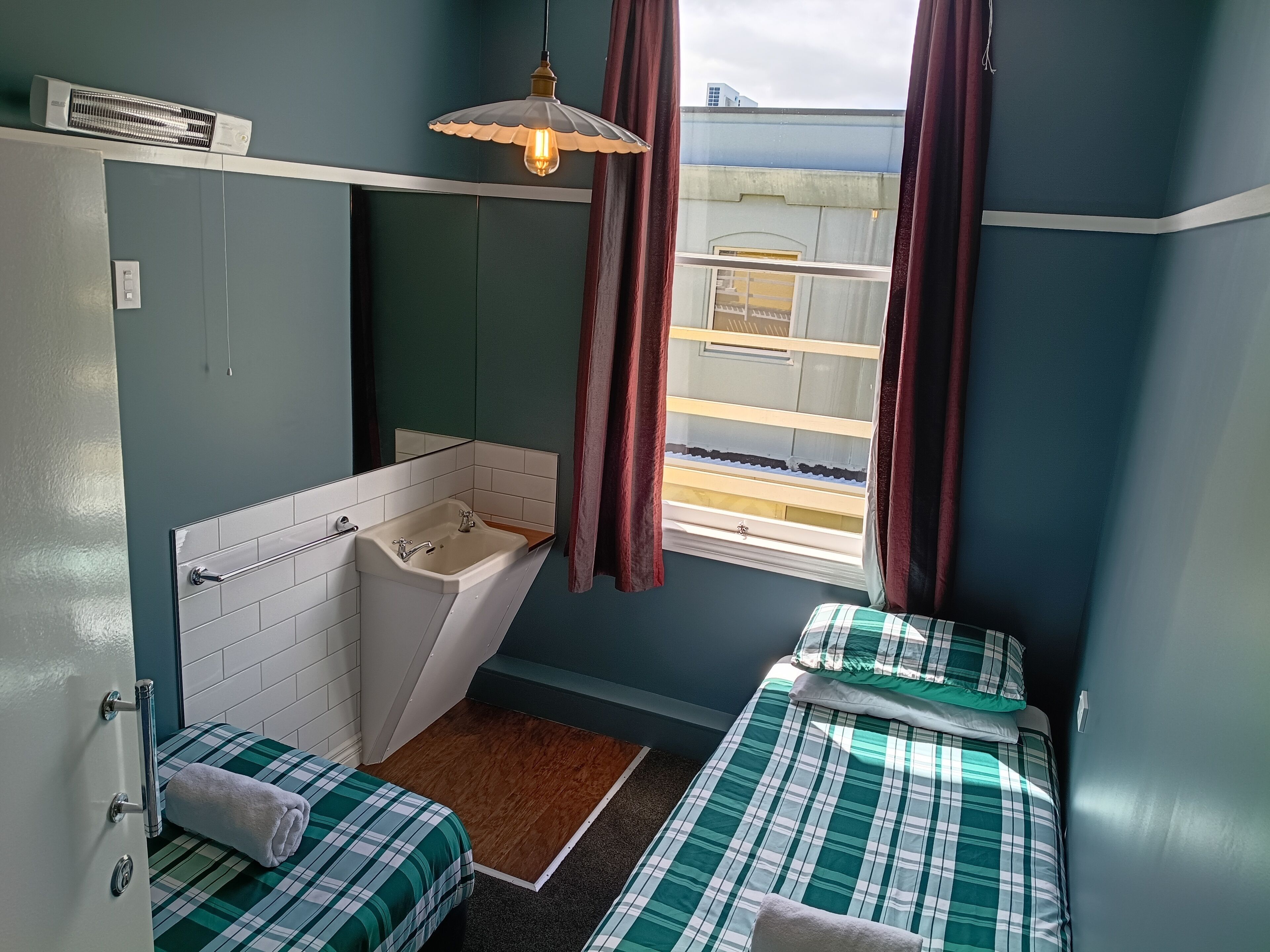 A compact room with a single bed, a small bathroom with a sink, and a window with curtains.