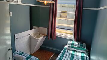 A compact room with a single bed, a small bathroom with a sink, and a window with curtains.