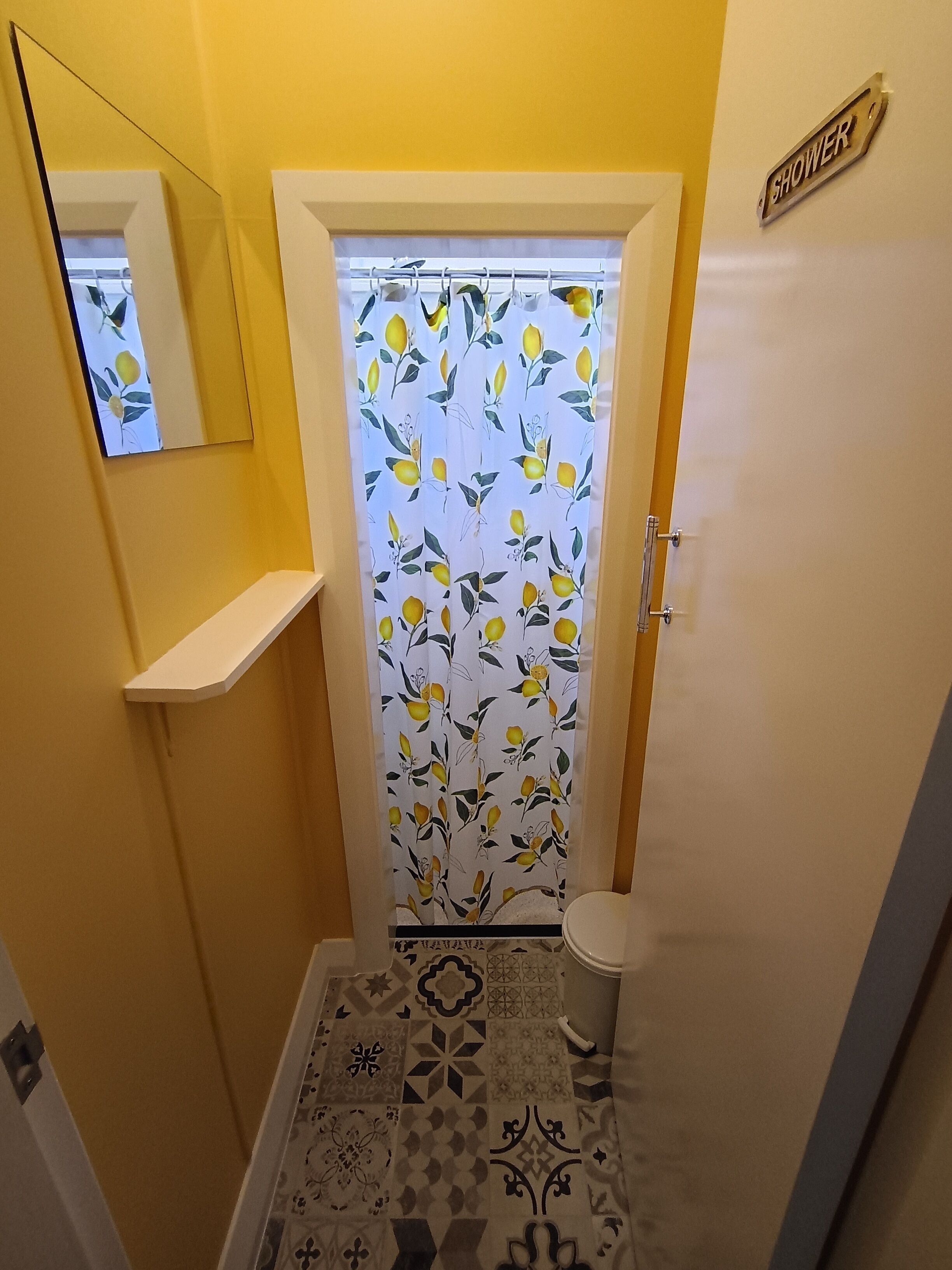 Un baño pequeño con cortina de ducha estampada con motivos de limón, un inodoro y un espejo en la pared.