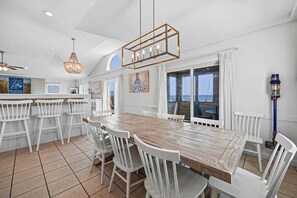 A spacious kitchen with a wooden table, white chairs, a chandelier, and a view of the ocean. - Sandfiddler | Oceanfront | Dog Friendly, Private Pool, Hot Tub | Nags Head (Nags Head)
