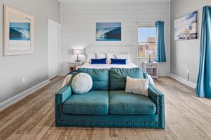 A bedroom with a bed, a teal sofa, and artwork on the walls. - Sandfiddler | Oceanfront | Dog Friendly, Private Pool, Hot Tub | Nags Head (Nags Head)
