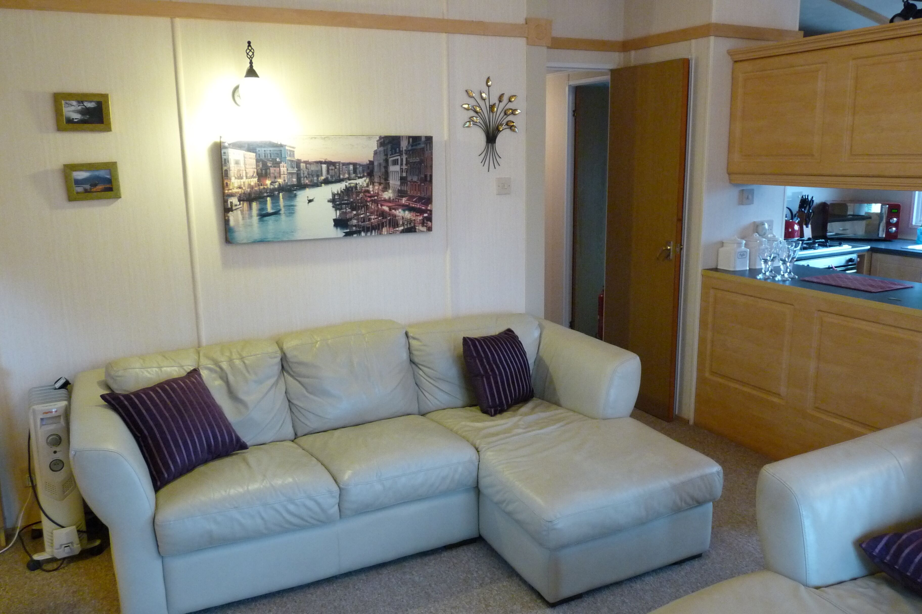 A living room with a light-colored leather sofa, a dining area with wooden cabinets, and a wall-mounted picture of a cityscape.