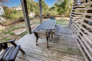 A wooden deck with picnic tables and chairs, surrounded by a wooden fence and greenery.