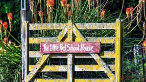 A rustic wooden gate with a sign that reads "The Little Red School House."