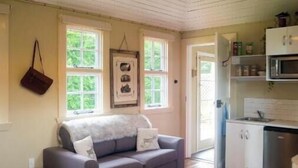 A cozy room with a sofa, a small table, a cowhide rug, and a kitchen area with cabinets and a microwave.