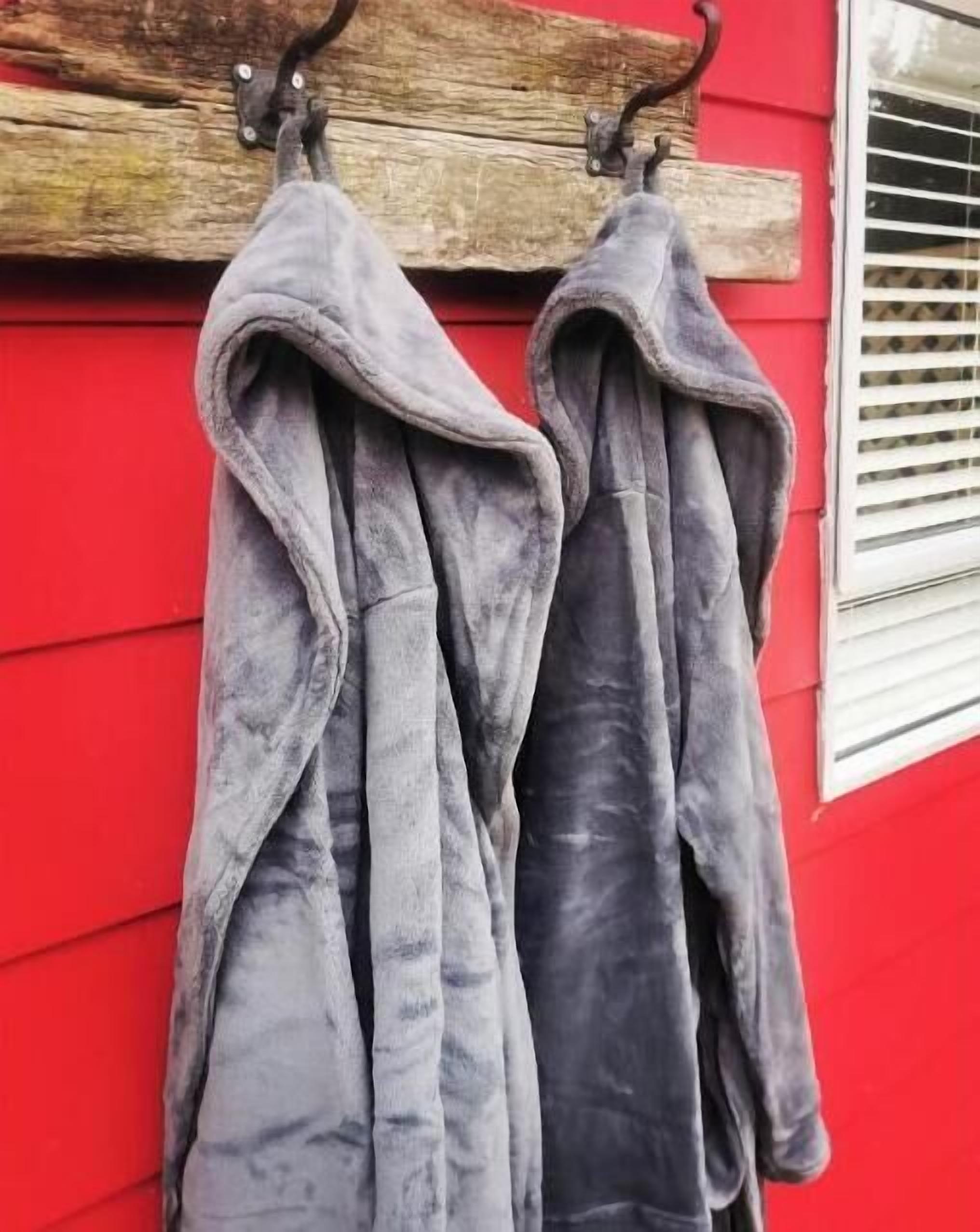 Two grey jackets hanging on a hook against a red wall.
