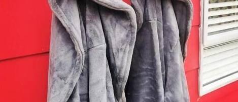 Two grey jackets hanging on a hook against a red wall.