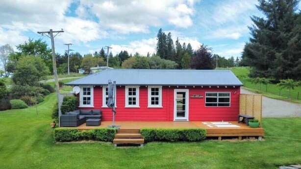 A red house with a porch, a small deck, and a lawn.