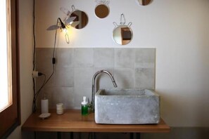 Ein Badezimmer mit einem rechteckigen Waschbecken, einem Spiegel und einer Wandleuchte.