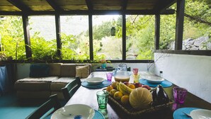 Un coin repas avec une table dressée pour deux personnes, entouré d’une pergola en bois offrant une vue sur une végétation luxuriante.