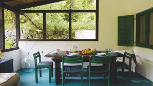 Un coin repas avec une table dressée pour quatre personnes, entourée de chaises, et offrant une vue sur la verdure à l’extérieur.