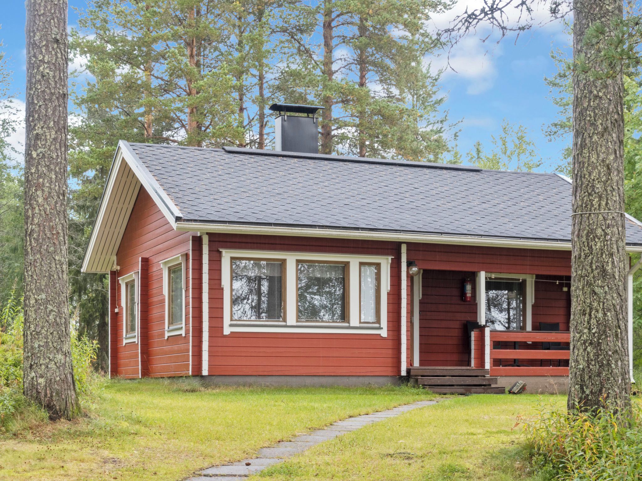 A red cabin with a chimney, a porch, and a pathway leading to the entrance.