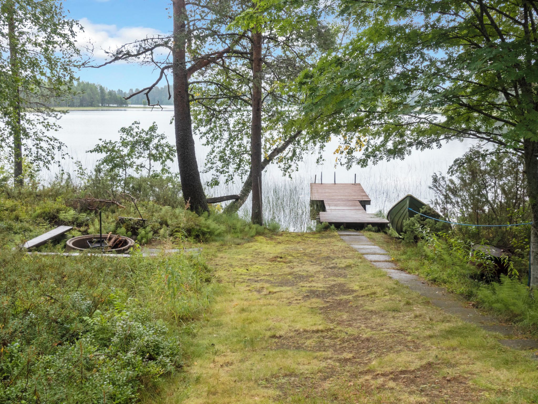 En träbrygga som sträcker sig ut i en sjö, omgiven av träd och tät vegetation.