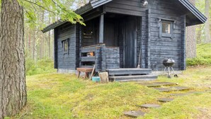 A rustic cabin with a porch, a small table, and a grill outside.