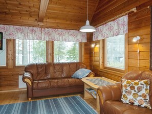 Interior acolhedor de uma cabana com um sofá de couro marrom, uma mesinha e uma poltrona com almofadas estampadas.